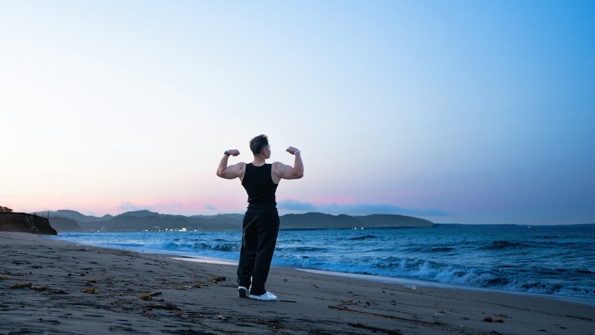 A person flexing muscles on a beach at sunset